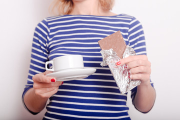 Hands holding chocolate and cup of drink on white background