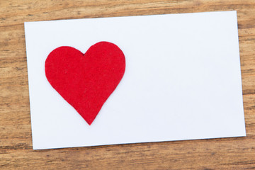 Blank sticky note with a red heart on a wooden background