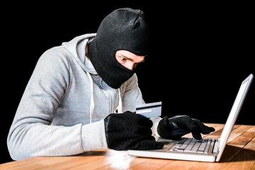 Focused thief with hood typing on laptop