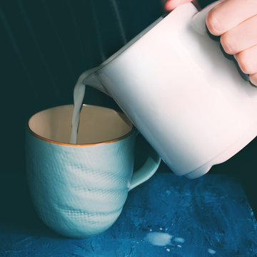 Pouring milk in a blue mug on dark blue background