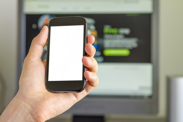 Closeup of man's hand holding smartphone in front of computer screen.