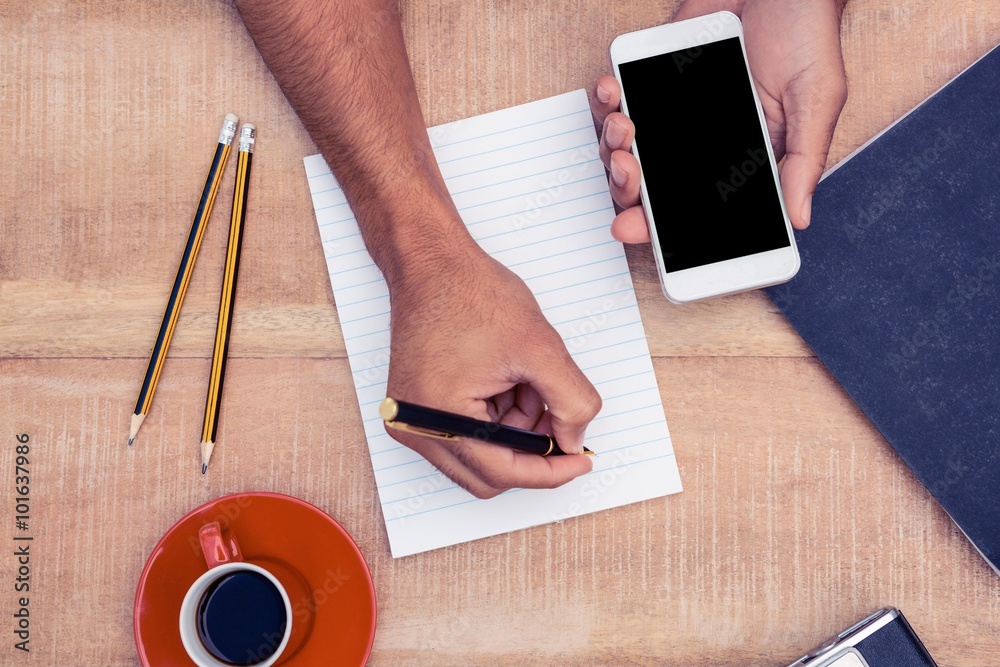 Poster overhead view of manholding smartphone while writing