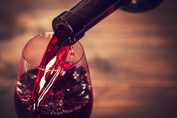 Pouring red wine into the glass against wooden background