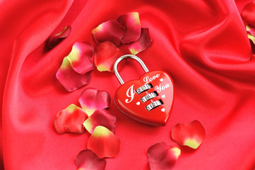 Padlock heart-shape on a background of red petals and satin