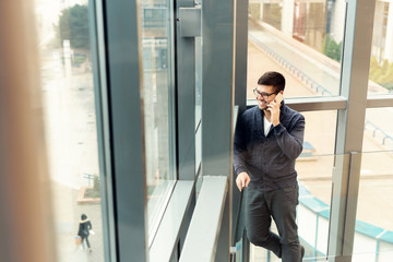 Casual businessman talking on smart phone. He is standing in front of a big window and looking outside.