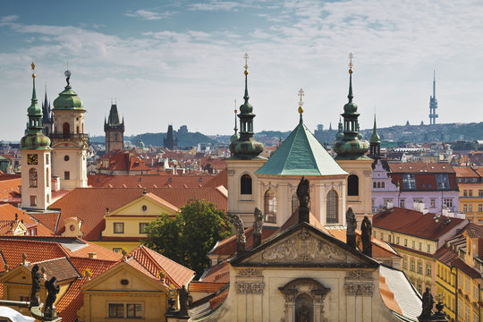 View of the roofs of Prague, with red tiled roofs and  statues, spires and towers protruding