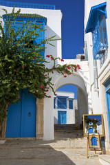 Fototapeta na wymiar Tunisia. Sidi Bou Said - typical building with white walls, blue doors and windows. Framed pictures (on easel) are taken by me 