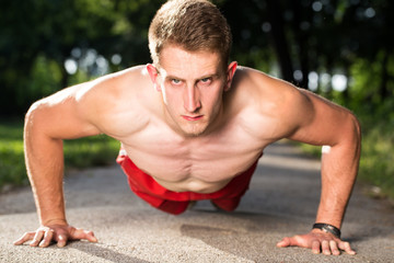 young muscular man push ups on walking road in a park  