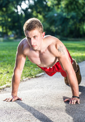 young muscular boy doing pushups on walking road in a park  
