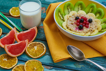 Healthy breakfast with oatmeal and fruit. Granola with kiwi, bananas, berries, grapefruit and a glass of milk. Wooden background. Selective focus