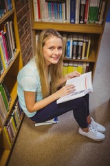 Blonde student reading while sitting on books