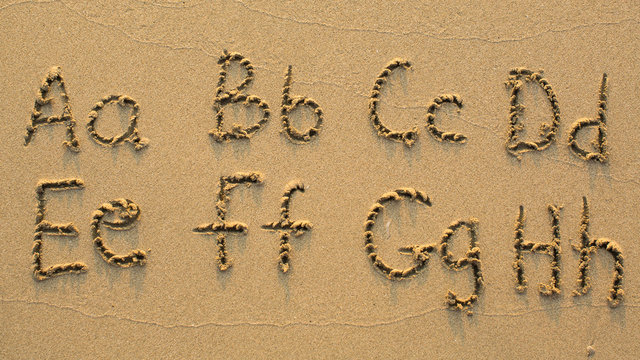 Letters of the alphabet written on sandy beach (from A to H)