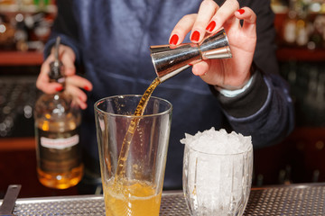 Female bartender is adding whisky to the glass