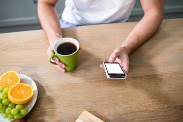 Handsome man using smartphone and holding cup