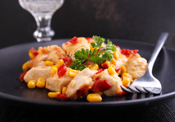 fried chicken with corn and sweet red peppers on a black plate