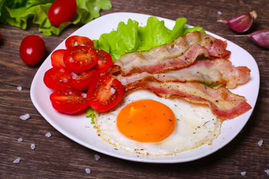 Hearty breakfast. Fried egg with bacon and tomatoes on a wooden background