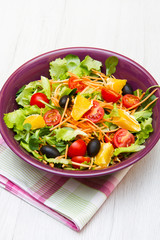 mixed salad with tomatoes in purple bowl on wood table