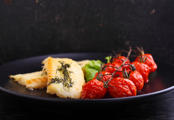 Grilled white fish fillet with baked tomatoes on the black plate