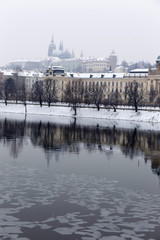 Snowy and foggy Prague Lesser Town with gothic Castle above river Vltava, Czech Republic