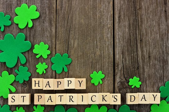 Happy St Patricks Day wooden blocks with corner border of shamrocks over a rustic wooden background