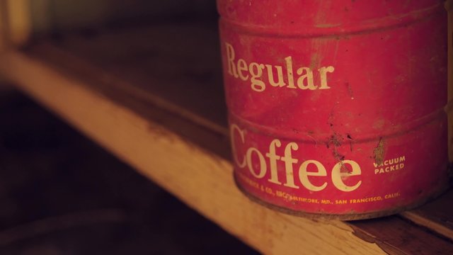 An old coffee can sits on a shelf in an abandoned cabin.