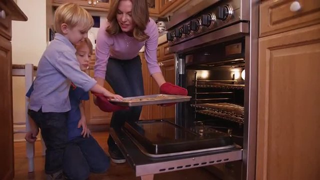 Beautiful white mother using oven mitts to remove cookie tray