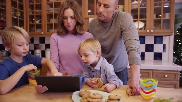 Happy family eating cookies and looking at a tablet computer