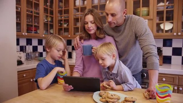 Two young brothers eating cookies and watching a tablet with parents