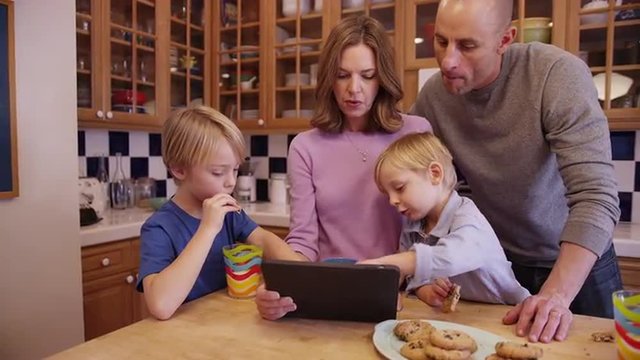 Two lovely caucasian parents eating cookies and reading a tablet with children