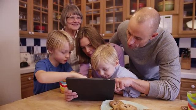 Happy family eating cookies while looking at a tablet computer