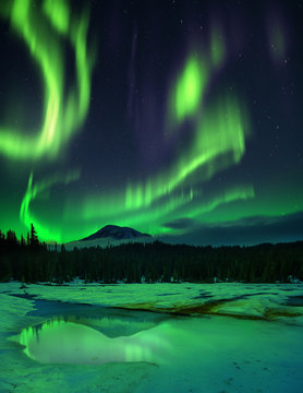 This is a photograph of night sky with aurora borealis and stars over frozen lake with reflections.