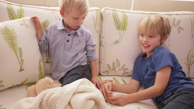 Young blond boy tickling his brother's feet on a sofa