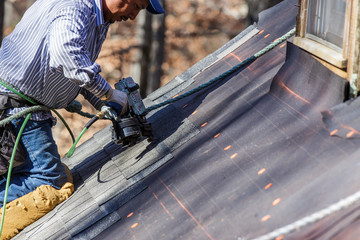 Roofer uses nail gun to secure shingles. - obrazy, fototapety, plakaty