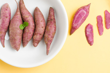 Raw sweet potatoes in the bowl on yellow pastel background