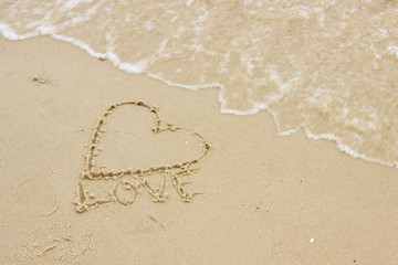 Fototapeta na wymiar Word love and heart written on sand at the beach by the sea
