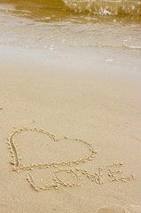 Word love and heart written on sand at the beach by the sea