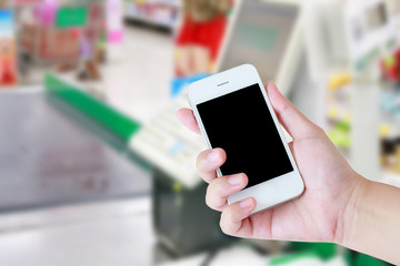 Hand holding mobile phone at supermarket checkout background