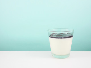 The tasty homemade blueberry panna cotta (Italian pudding dessert) in the small glass on white table.