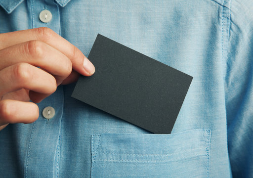 Young man who takes out black blank business card from the pocket of his shirt