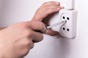 male hands with screwdriver installing electrical socket on wall