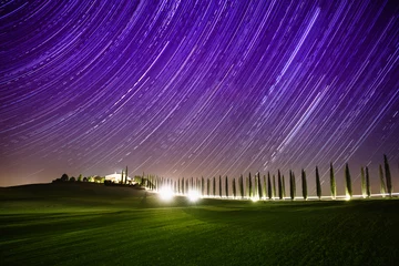 Papier Peint photo Violet Beau paysage nocturne de Toscane avec des traînées d& 39 étoiles dans le ciel, des cyprès et une route brillante dans un pré vert. Fond de fantaisie incroyable en plein air naturel.