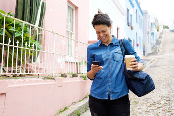 Smiling young woman walking with mobile phone and bag