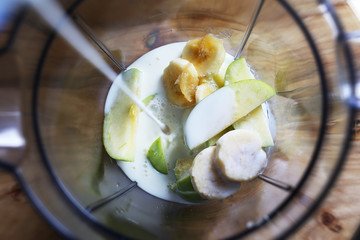 Pouring milk over bananas and apples in a blender. Making healthy shake.

