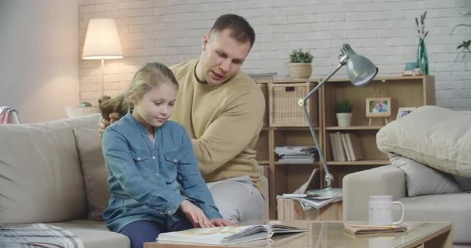 Daddy doing hair of his daughter while reading her a fairy tale