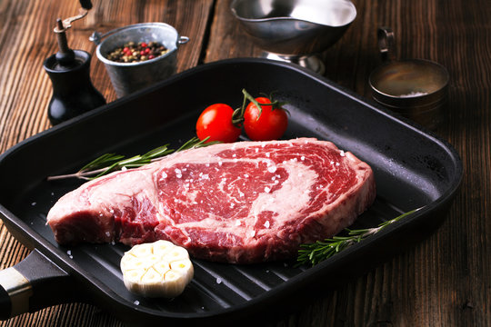 Raw beef steak marbled ribeye in a pan with rosemary, garlic and