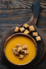Pumpkin soup served with croutons on a wooden chopping board