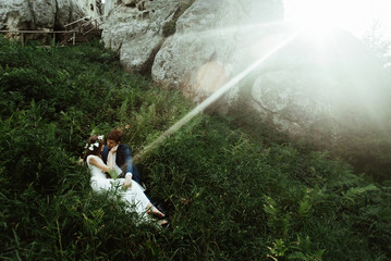 luxury happy bride and stylish groom lying on grass under sunny