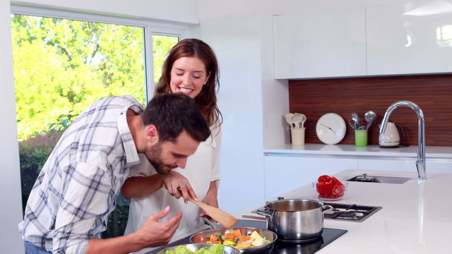 Happy man reaching his wife while she is cooking
