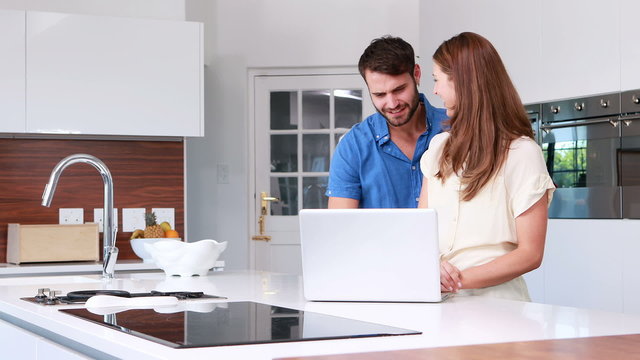 Happy couple using laptop in the kitchen
