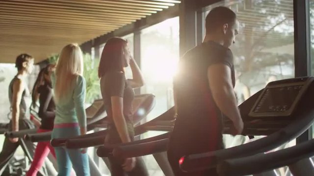 Young athletic men and women exercising and running on treadmill in sport gym. Shot on RED Cinema Camera.